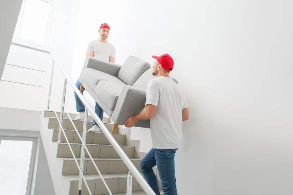 Två män bär en soffa uppför en trappa